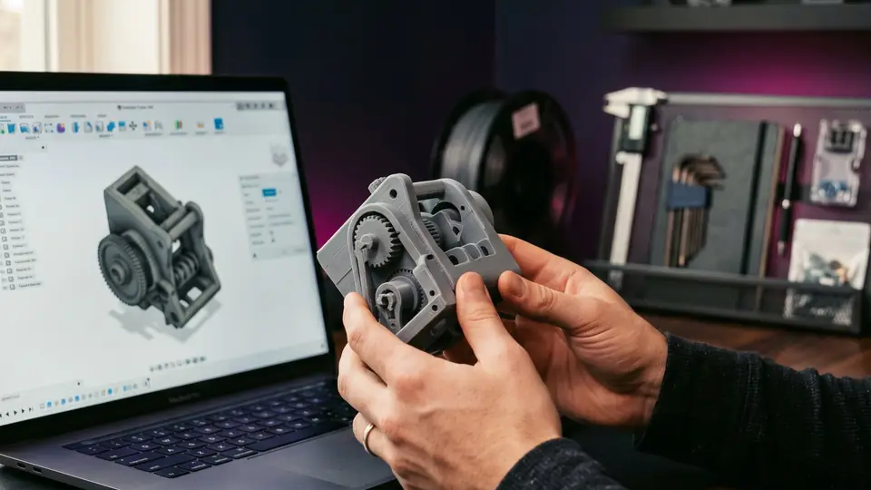 Person comparing a printed part with its 3D model on a laptop